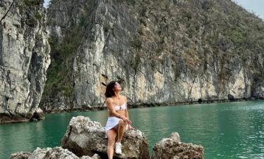 Stunning woman sitting on rocks by emerald water in Halong Bay, Vietnam.