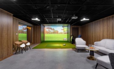 Indoor golf simulator room with high-tech screen and comfortable seating, perfect for golf practice and entertainment.