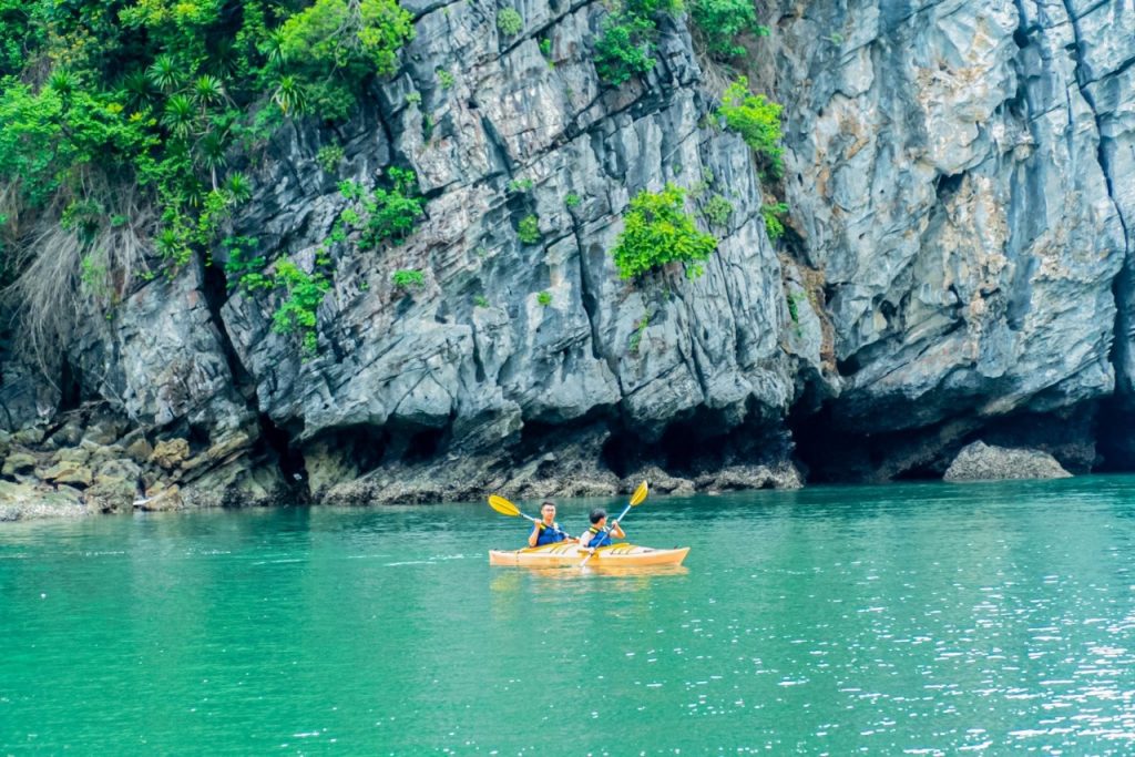 Beautiful kayaking tour in emerald waters surrounded by lush green cliffs in Vietnam.