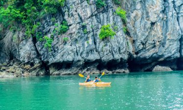 Beautiful kayaking tour in emerald waters surrounded by lush green cliffs in Vietnam.