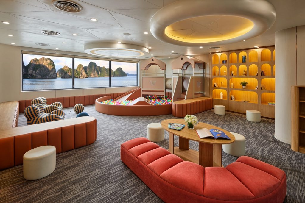 Playroom with sea view, ball pit, cozy seating, wooden shelves, and scenic ocean landscape in background.