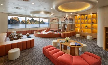 Playroom with sea view, ball pit, cozy seating, wooden shelves, and scenic ocean landscape in background.