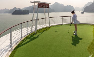 A girl playing mini golf on a scenic outdoor course overlooking a bay with limestone islands.