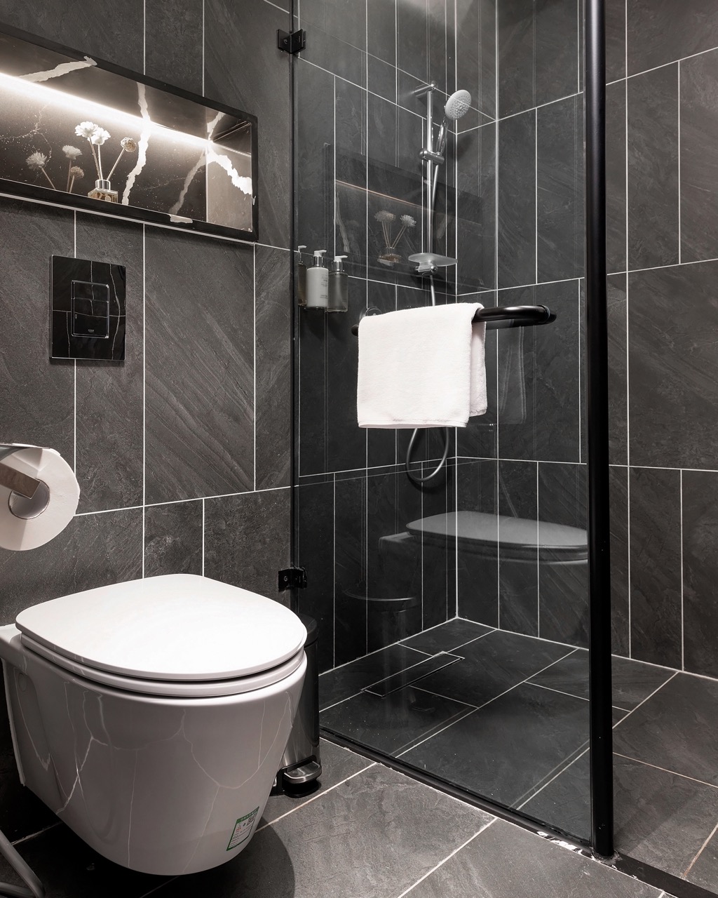 Modern black-tiled bathroom with walk-in shower and sleek toilet, stylish design, perfect for luxury accommodation.