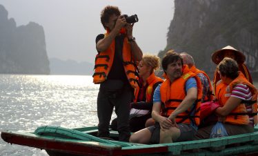 An Asian woman taking photos of tourists on a boat tour in Ha Long Bay, Vietnam.