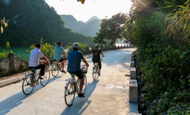 Bicyclists enjoying scenic countryside tour along river in Vietnam during sunny day.