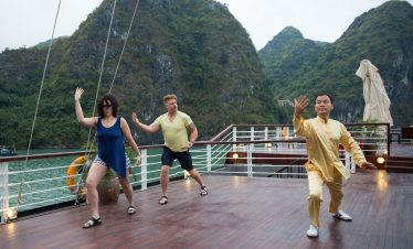 Relaxing Tai Chi session on a cruise deck with lush green mountains in Vietnam's Ha Long Bay.