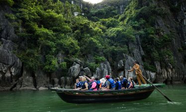 Boat tour through Ha Long Bay with tourists exploring limestone karsts, lush greenery, and emerald waters in Vietnam.