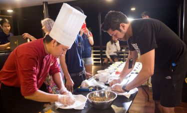 Chef in traditional outfit and a man preparing food at a Vietnamese cuisine cooking class.