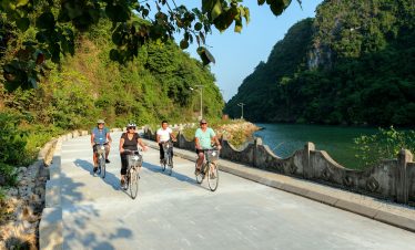 Cyclists riding along a scenic river route surrounded by lush green mountains in Vietnam.