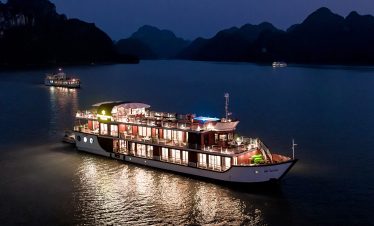 Luxury cruise ship on Halong Bay at night with illuminated decks and scenic mountain backdrop.