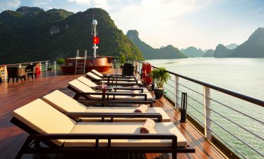 Relaxing cruise deck with sun loungers overlooking scenic limestone islands in Ha Long Bay, Vietnam.