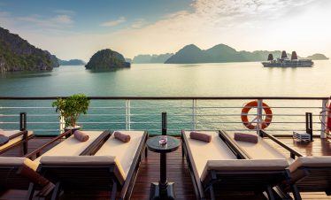 Relaxing cruise deck with sun loungers overlooking Ha Long Bay's scenic karst islands in Vietnam.
