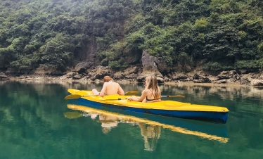 Women kayaking in calm green water surrounded by lush forest, Vietnam travel adventure.