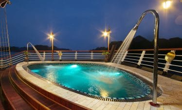 Outdoor hot tub on a cruise ship deck with scenic mountain backdrop at dusk.