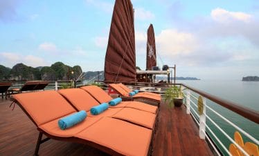 Relaxing boat cruise deck with sun loungers and scenic limestone islands in Vietnam.