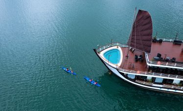Luxury cruise boat with private pool and kayak on emerald water in Ha Long Bay.