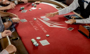 Exciting poker game at Delance Cruise Poker Club with players and dealer on a red felt table.