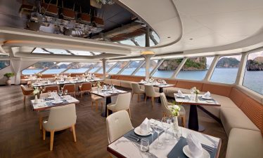 Luxurious cruise ship dining area overlooking ocean with modern decor and elegant table settings.