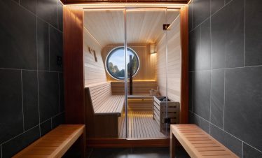 Relaxing sauna with wooden interiors and mountain view through round window.