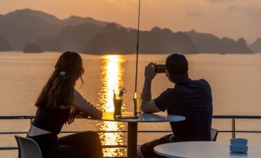 Sunset cruise on Halong Bay with couple enjoying romantic scenery and drinks.