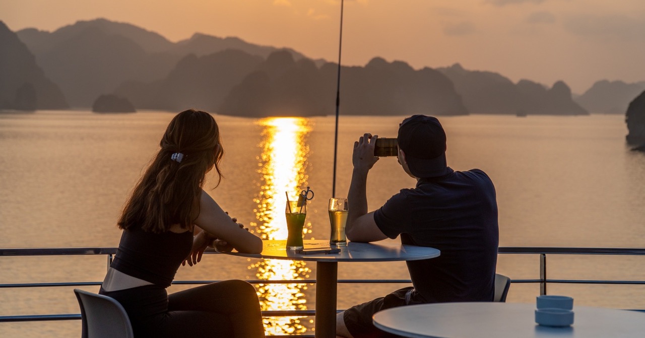 Sunset cruise on Halong Bay with couple enjoying romantic scenery and drinks.