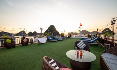 Stunning terrace view with lounging chairs and string lights over Halong Bay at sunset.