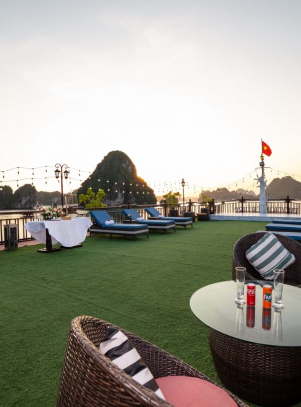 Stunning terrace view with lounging chairs and string lights over Halong Bay at sunset.