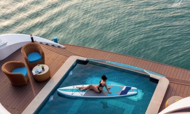 Woman relaxing on paddleboard in infinity pool overlooking the sea, luxury yacht cruise experience.