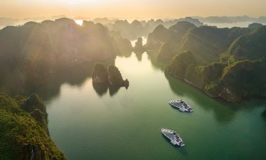 Vietnameses natural landscape with limestone karsts and cruising boats at sunset.