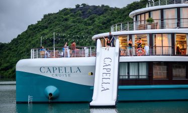 Luxurious Capella Cruise ship on the water with scenic green hills in the background.