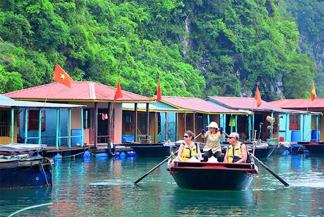 Colorful floating houses in Halong Bay, Vietnam, with tourists enjoying boat tours and scenic views.