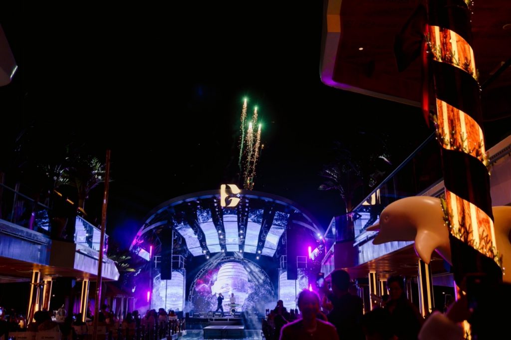 Firework display at night during a live outdoor music event with colorful stage lighting.