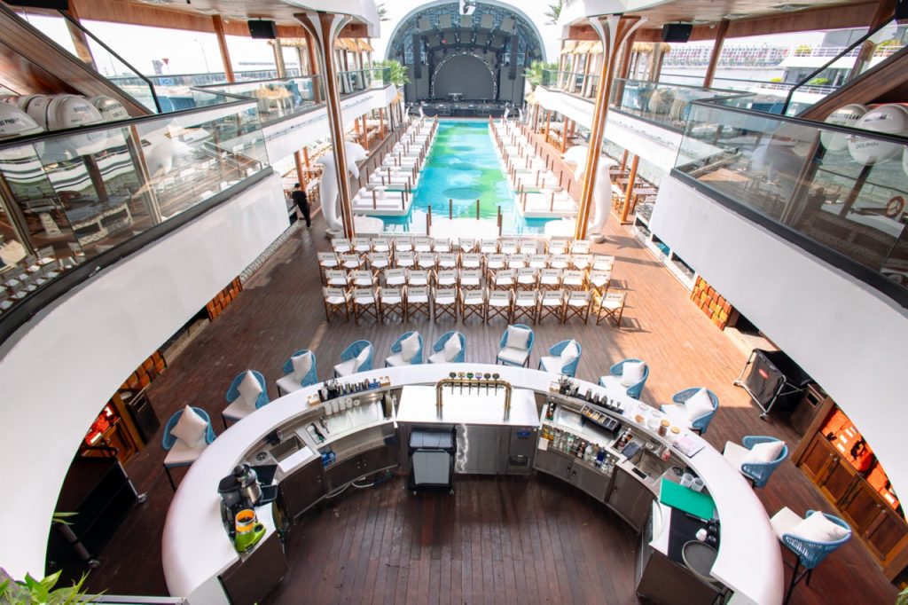 Luxury cruise ship deck with swimming pool, bar, and panoramic views.