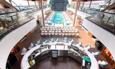 Luxury cruise ship deck with swimming pool, bar, and panoramic views.