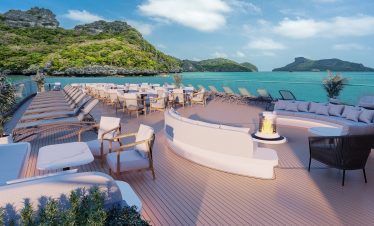 Luxurious oceanview cruise deck with lounge chairs and fire pit in tropical paradise.