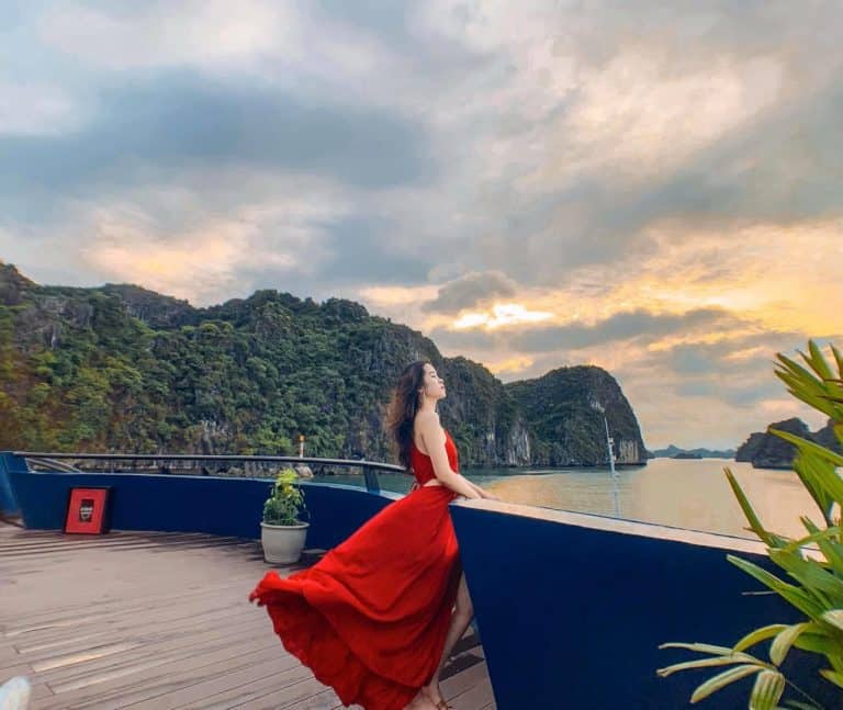 Lan Ha Bay Cruise 1 Night - Stunning Halong Bay scenery with a woman enjoying the sunset from a cruise balcony, capturing the tr.