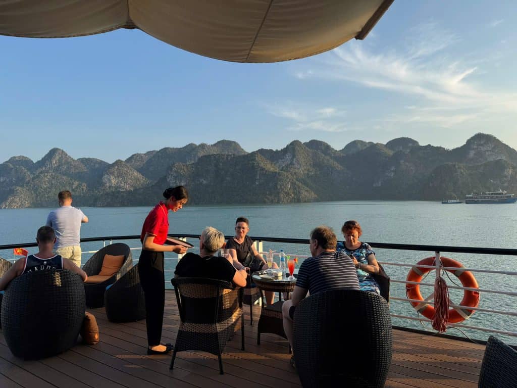 Relaxing cruise on Halong Bay with panoramic views of limestone karsts and a group enjoying dinner.
