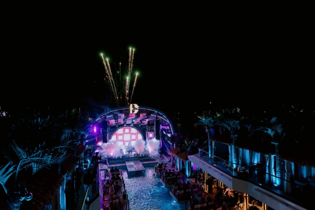 Nighttime music festival at a tropical resort with fireworks, colorful lights, and outdoor seating.