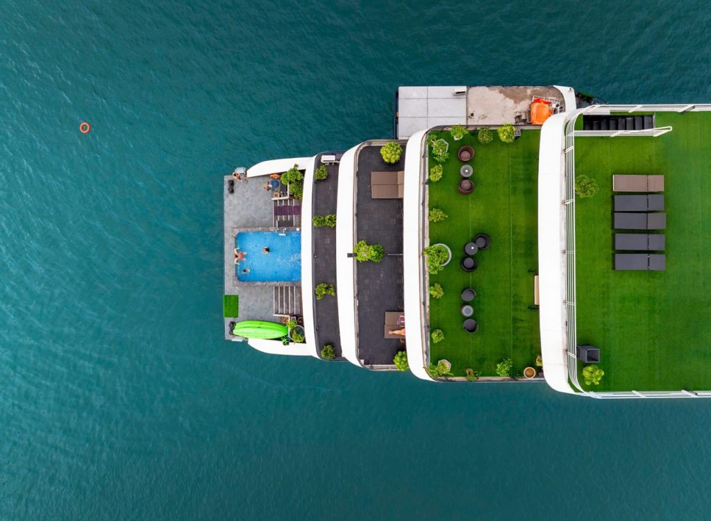 Aerial view of a luxury cruise ship with a pool and green deck, sailing in Lan Ha Bay, Vietnam.