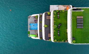 Aerial view of a luxury cruise ship with a pool and green deck, sailing in Lan Ha Bay, Vietnam.