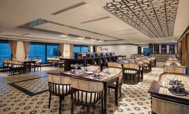 Luxurious cruise dining room with panoramic Lan Ha Bay views, elegant table settings, and modern dec.