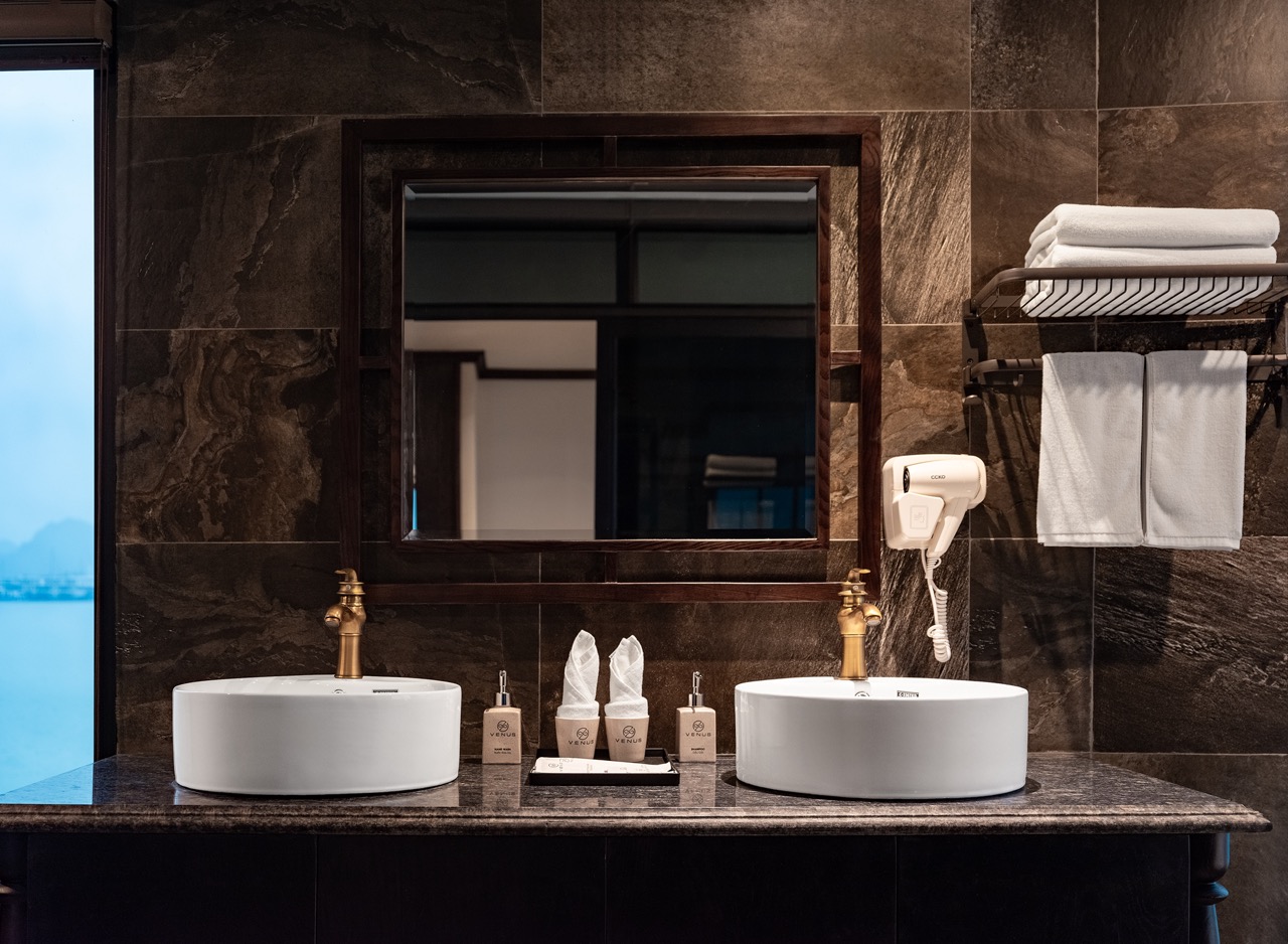 Luxurious cruise bathroom featuring twin sinks, stylish decor, and premium toiletries on Lan Ha Bay.