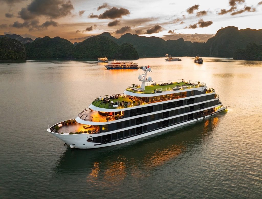 Luxury cruise ship sailing in Lan Ha Bay with scenic limestone karsts at sunset.