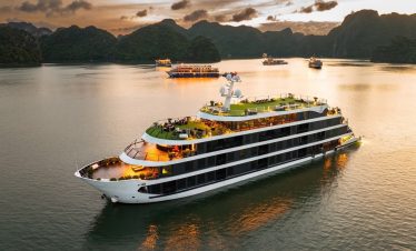 Luxury cruise ship sailing in Lan Ha Bay with scenic limestone karsts at sunset.
