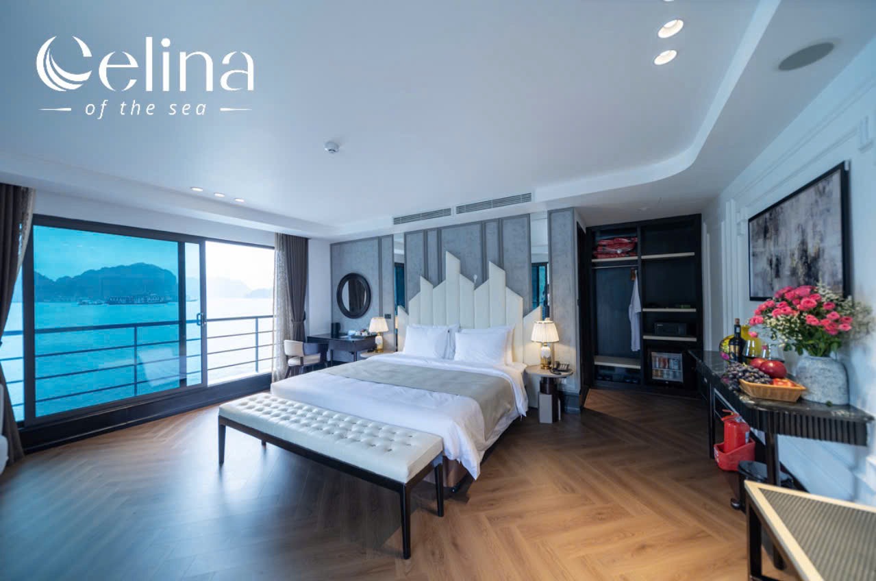 Luxurious hotel room with a king bed, bench at foot, and a sea view through a large window. Manual curtains frame the scene.