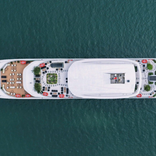 Aerial view of a large white luxury yacht cruising on calm blue water, seen from above.