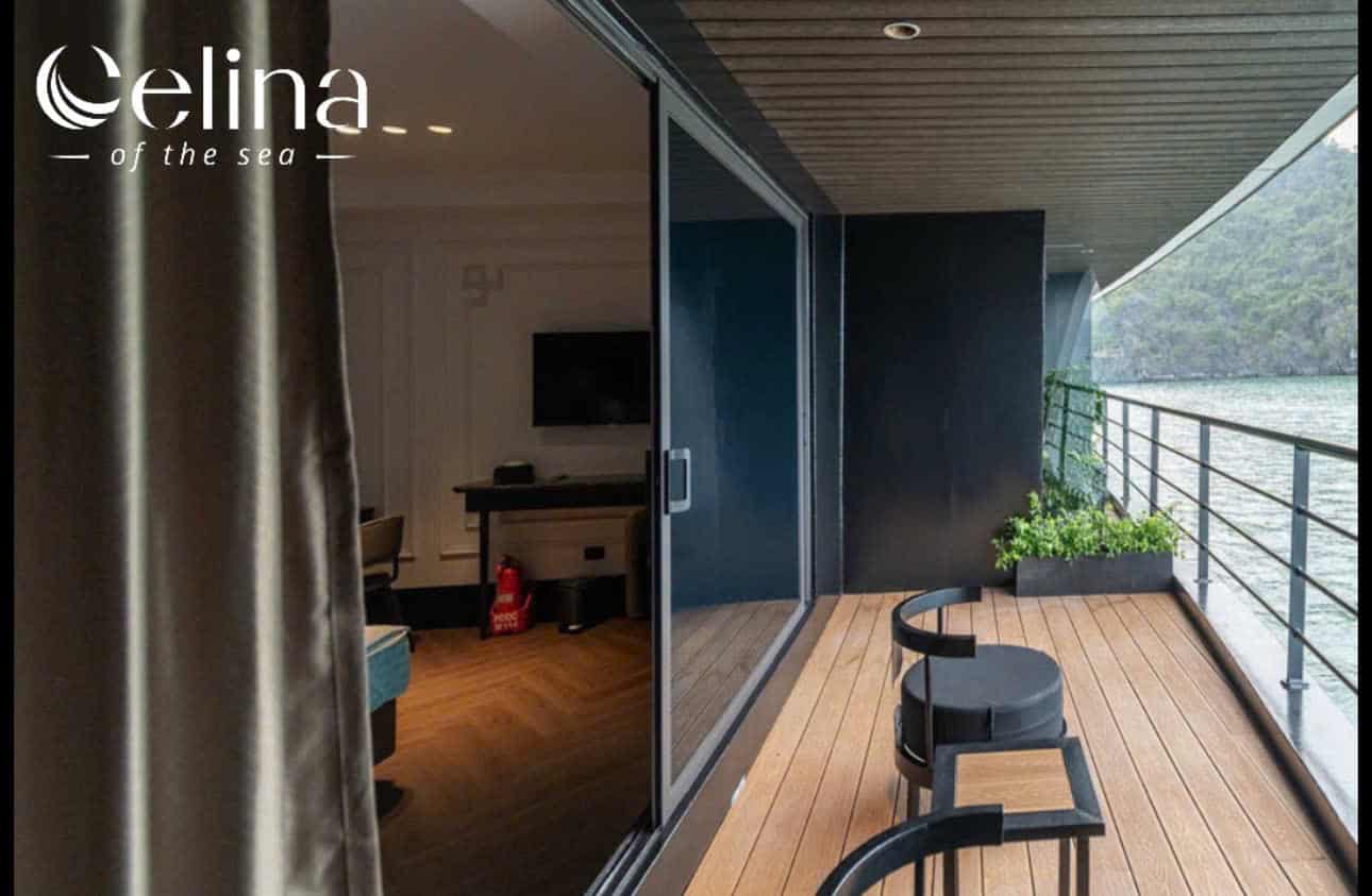 Balcony of a waterfront hotel with a wooden deck, glass sliding doors, and two black chairs, overlooking the water; logo 'celina of the sea' in the upper left.