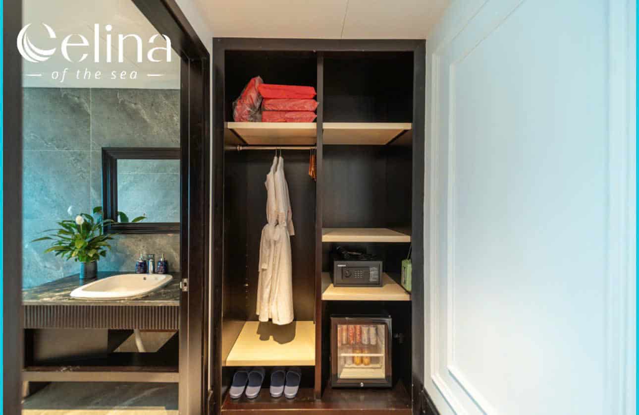 Closet area with a hanging robe, shelves, a safe, minibar, and slippers on the floor; sink area visible to the left; watermark 'Celina of the sea' in the corner