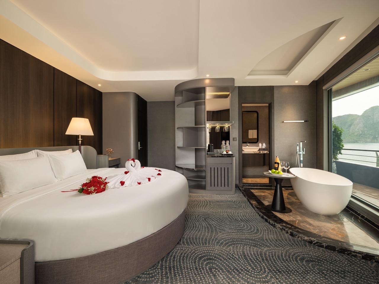 Luxurious hotel suite with a round bed decorated with rose petals and towel swans.